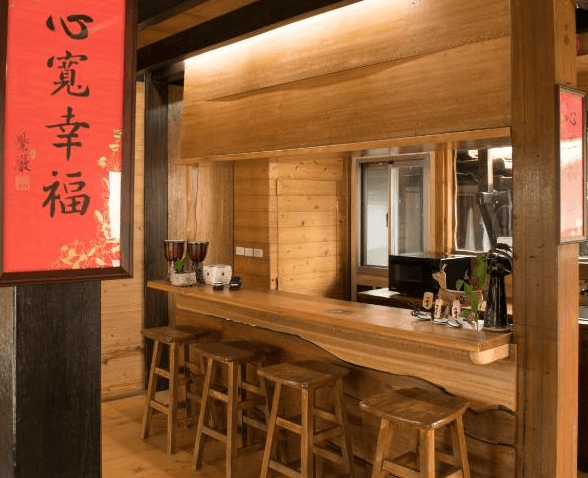【台東成功住宿】台東「比西里岸營地渡假小木屋」室內吧檯區，設有原木吧檯與高腳椅，牆上掛有紅色書法裝飾「心寬幸福」，整體充滿溫暖的木屋氛圍。