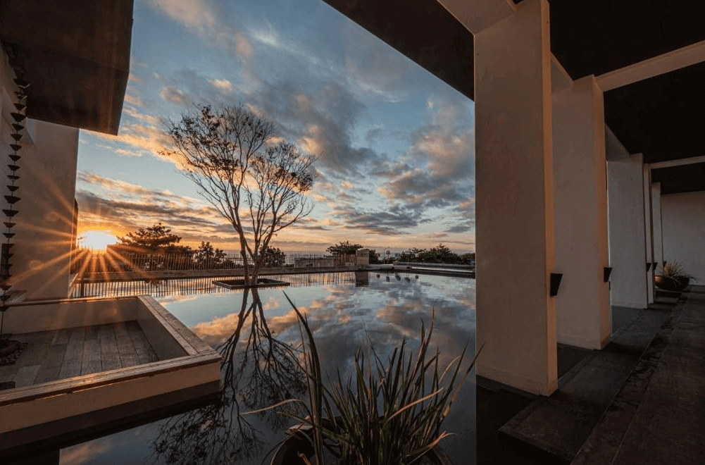 【豐濱住宿】夕陽餘暉灑落於水樹 AQUATREE RESORT 的鏡面水池中，搭配建築柱廊與倒映的樹影，畫面如詩如畫，展現寧靜而充滿藝術感的自然之美，是度假時刻不可錯過的風景。