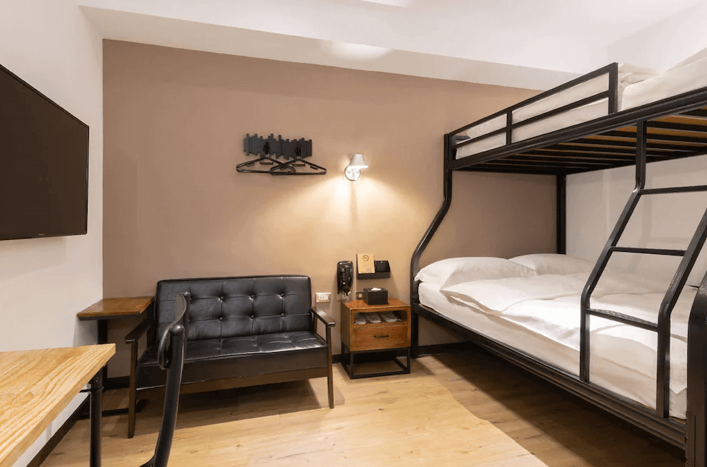 【高雄寵物友善住宿】河堤漫旅 站前館，有上下舖床位的四人房，床架為黑色金屬材質，底層為雙人床、上層為單人床，房內另有黑色皮沙發與木質書桌，風格工業且實用。