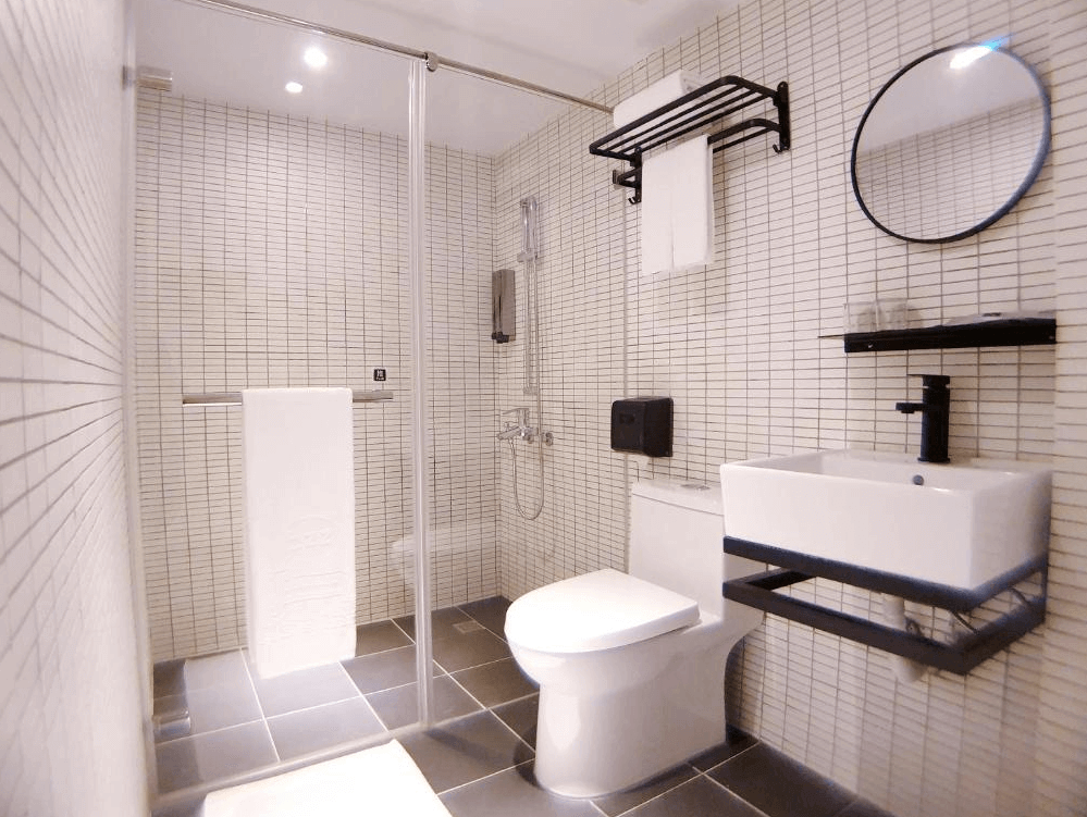 【高雄寵物友善住宿】河堤漫旅 站前館的衛浴空間，採乾濕分離設計，白色磁磚搭配黑色衛浴五金，設有玻璃隔間淋浴區、馬桶與洗手台，整潔明亮、實用性高。