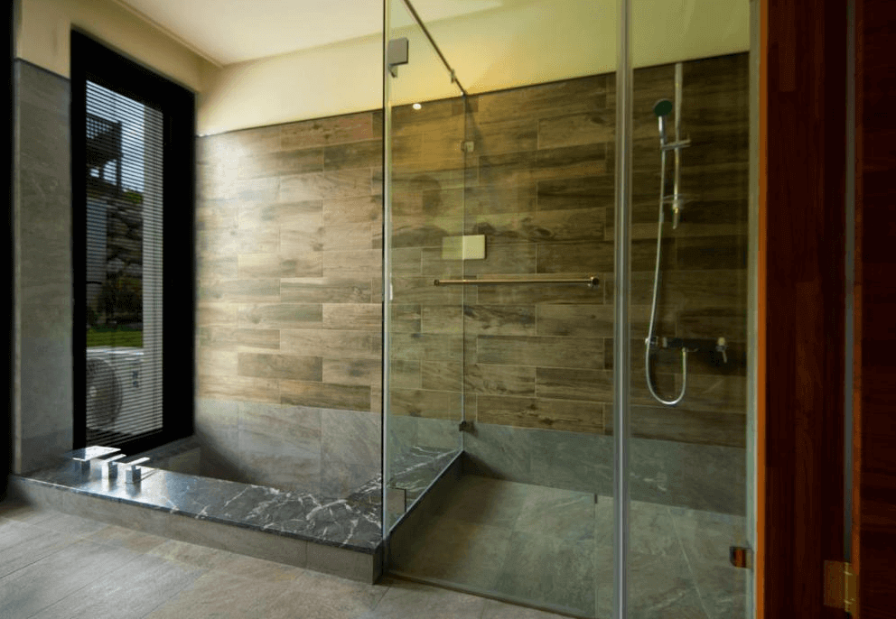 【長濱住宿】海Villa 胆曼會館衛浴空間，採用大片玻璃乾濕分離設計，牆面以木紋磁磚鋪設，自然採光良好並可望向戶外綠意。