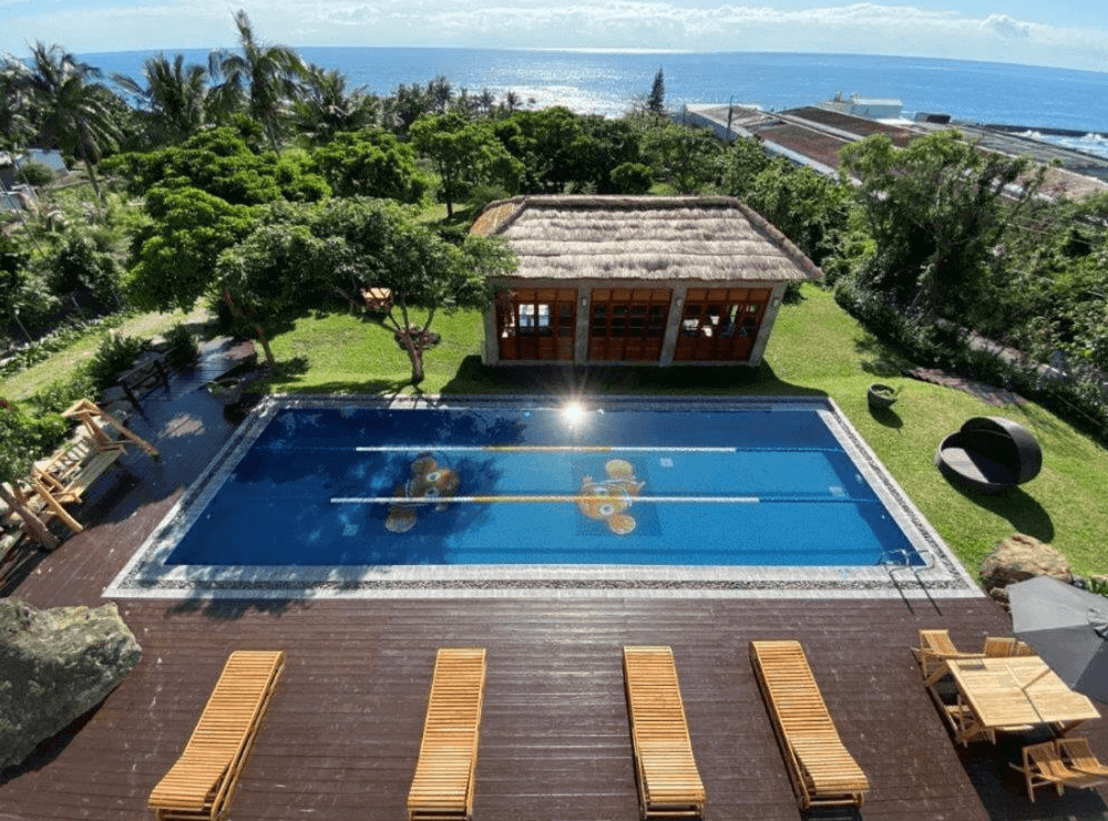 【長濱住宿】海Villa 胆曼會館戶外泳池與休憩草坪，設有多張躺椅與茅草屋風格的小屋，周圍綠樹環繞，可遠眺太平洋海景，盡享靜謐自然。