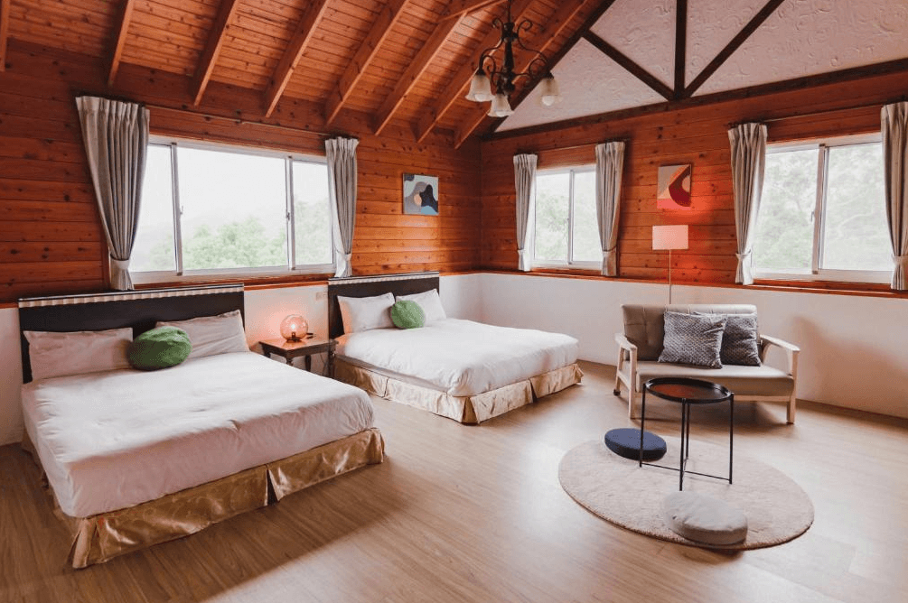 【苗栗包棟民宿】福田瓦舍 Villa，擁有挑高斜屋頂與木質牆面的雙床家庭房，配備兩張舒適雙人床與沙發小茶几，窗戶環繞四側，採光極佳，展現溫馨木屋氛圍。