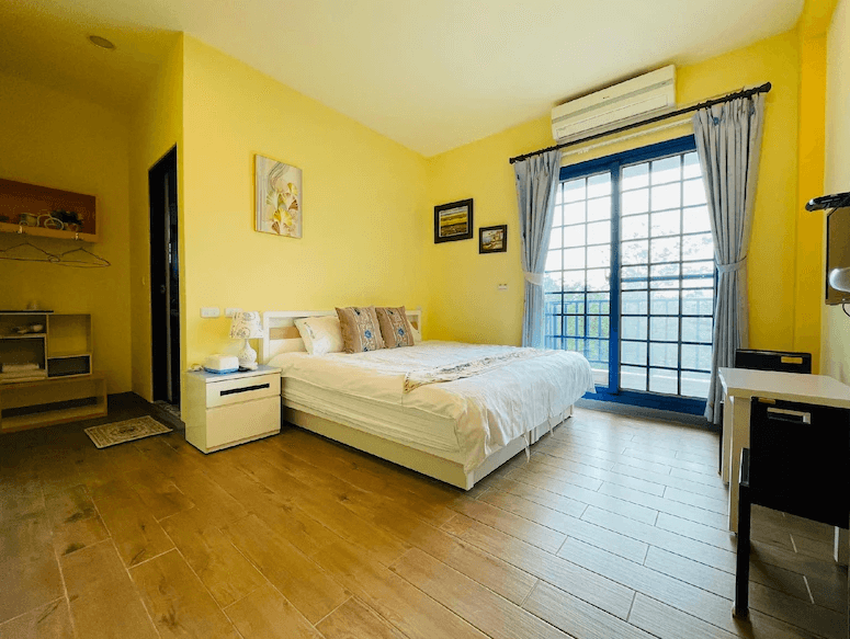 【關山住宿】稻香田園民宿的雙人房型，牆面採活潑明亮的鵝黃色調，搭配原木地板與藍色窗框，整體風格清新溫暖，窗外陽台可眺望田園景色。