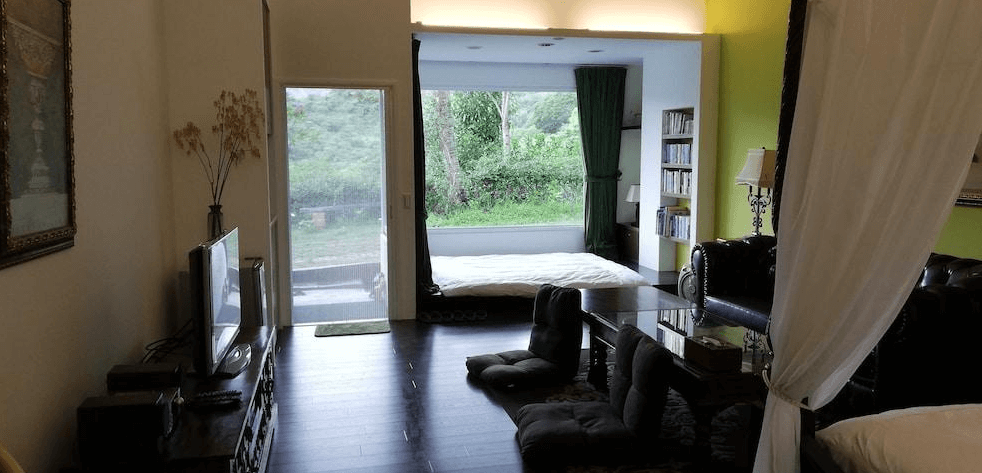 【長濱住宿】竹湖山居民宿客廳與臥室連通空間，設有日式榻榻米休憩區與大片窗景，外望綠意盎然的山林景觀，環境靜謐自然。