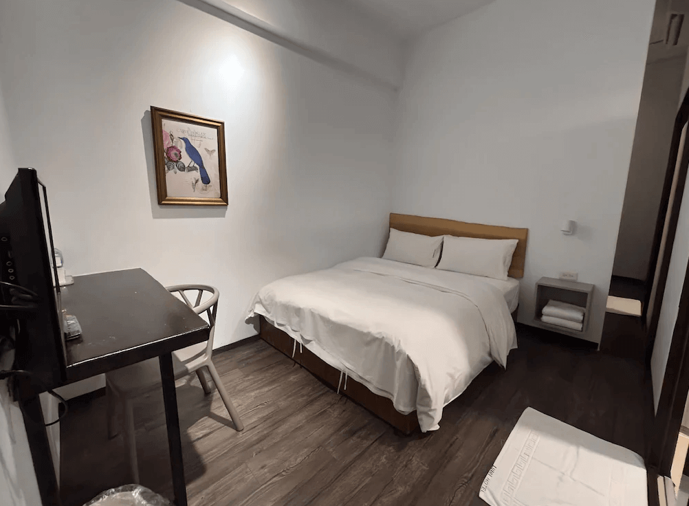 【Xpark住宿】綠藤輕旅溫馨雙人房，配有木質床架、柔軟白色床鋪與黑色書桌椅，牆上掛有藝術畫作，營造雅緻氛圍。
