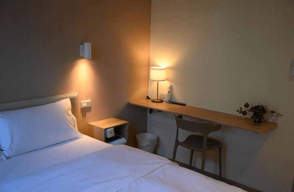 【Xpark住宿】綠藤輕旅單人房一隅，燈光柔和溫暖，木質書桌上擺有檯燈與裝飾植物，簡潔實用的設計適合短暫停留與放鬆。