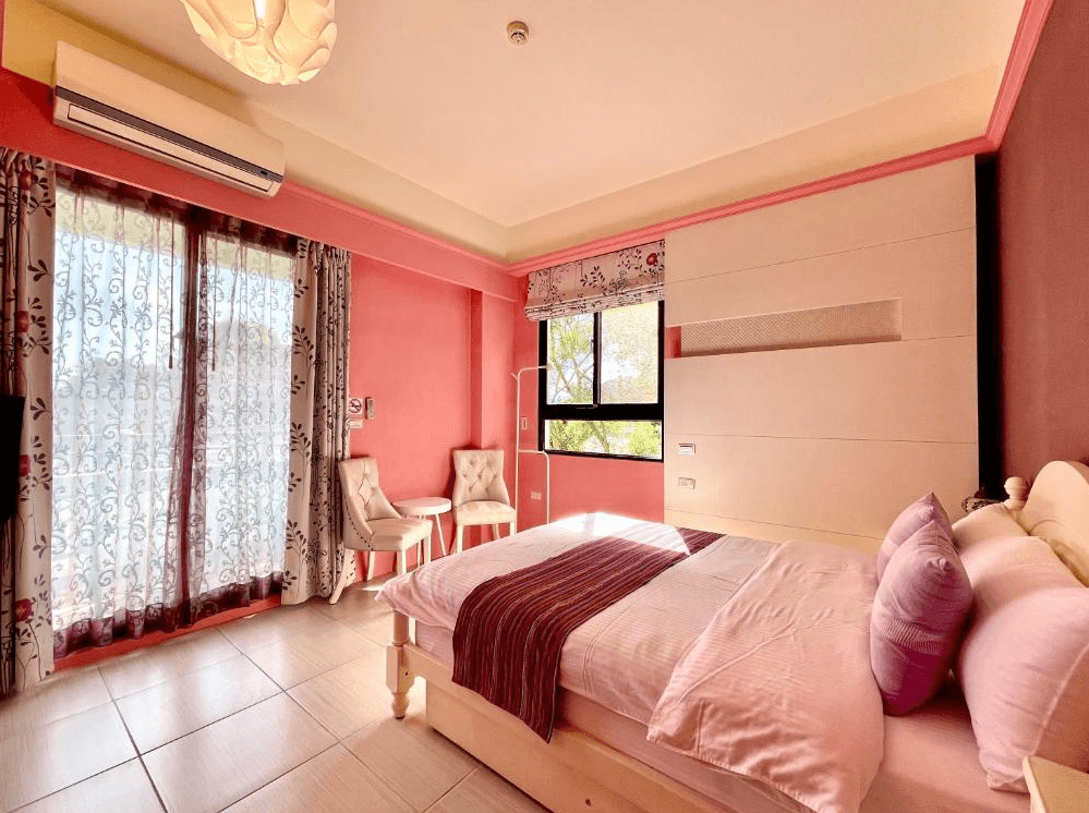 【關山住宿】纏民宿 x Remindful 的粉紅主題雙人房，採柔和色調搭配紫色抱枕與窗簾花紋，設有對坐小茶椅與大片落地窗，空間溫馨舒適。