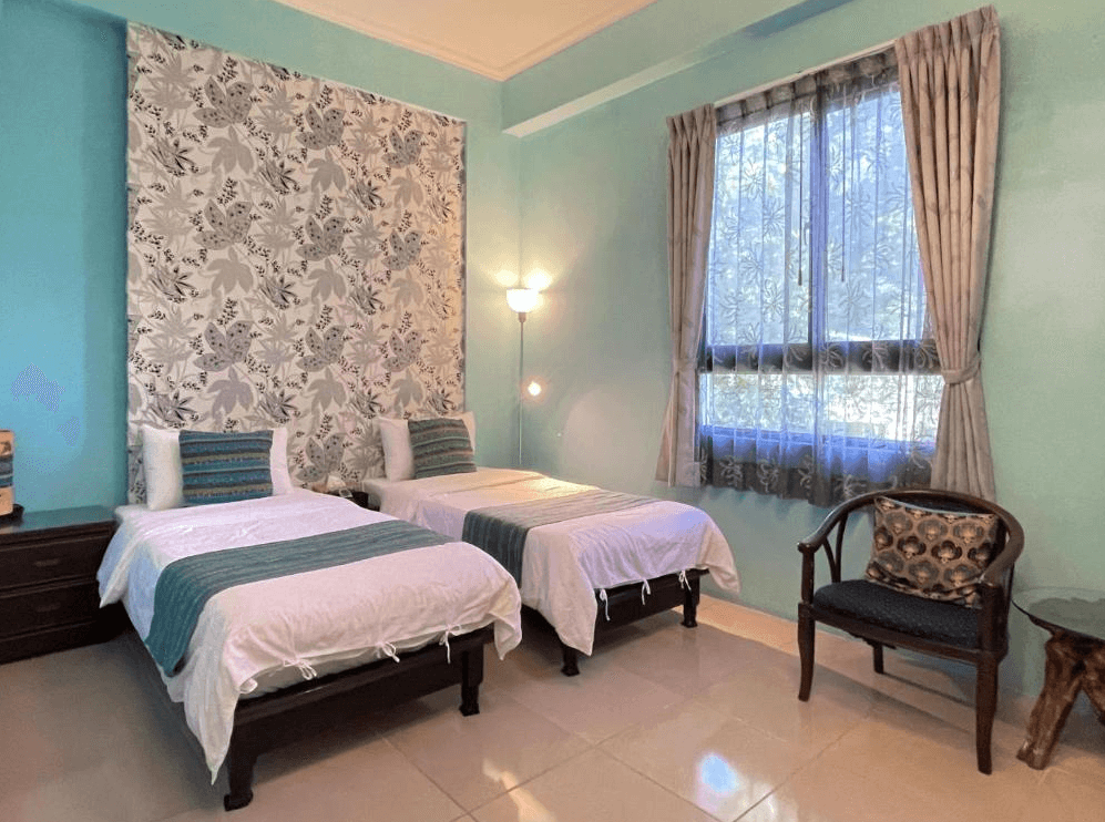 【關山住宿】纏民宿 x Remindful 的雙床房型，牆面以天藍與灰綠搭配葉紋布幕，風格典雅自然，備有古典木椅與小茶几，適合好友或親子入住。