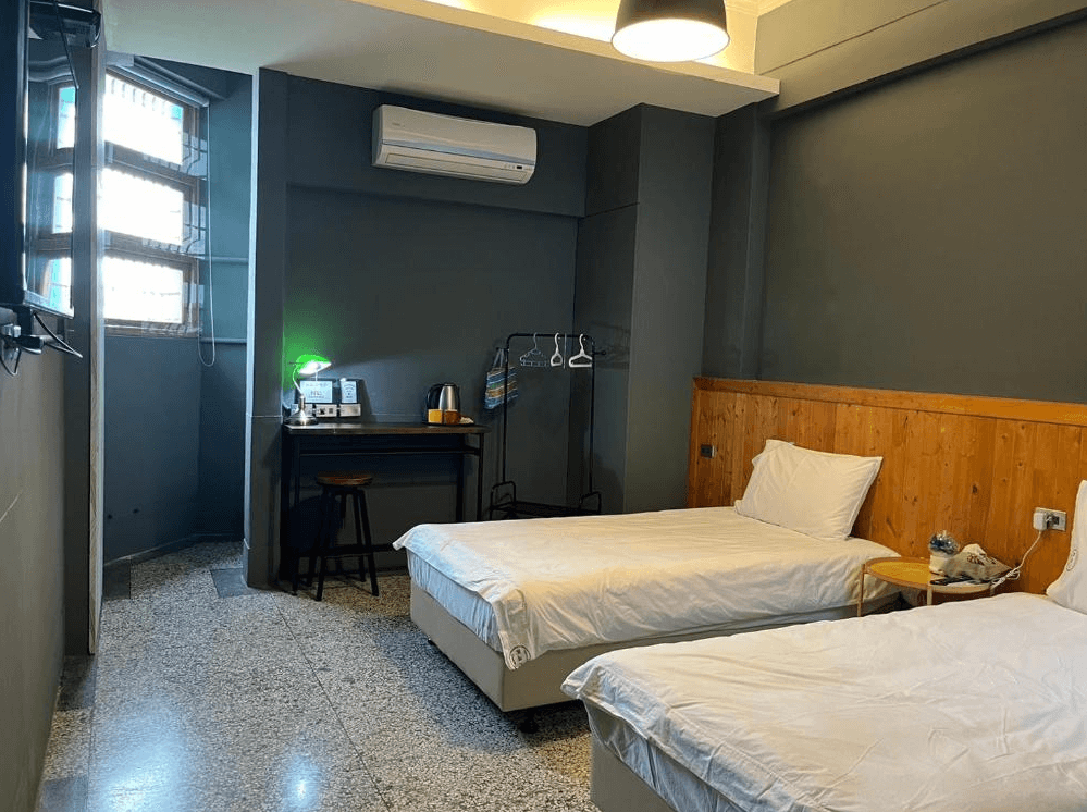 【關山住宿】興源行民宿的雙床房，牆面為深灰色調，搭配木質床板與書桌，空間內附有基本備品與吊掛衣架，風格簡約帶有工業質感。