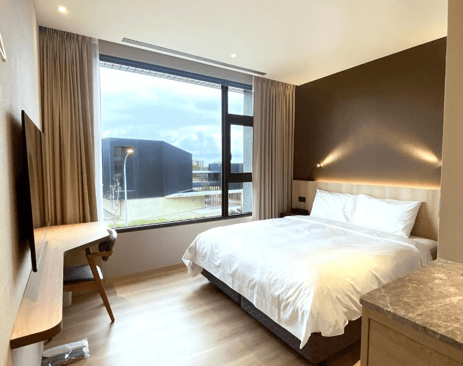 【桃園機場住宿】"Xpark住宿"艾爾芙公園行旅的標準雙人房，設有大片落地窗與簡約木質傢俱，房內空間明亮，窗外可見現代建築與綠地景觀。