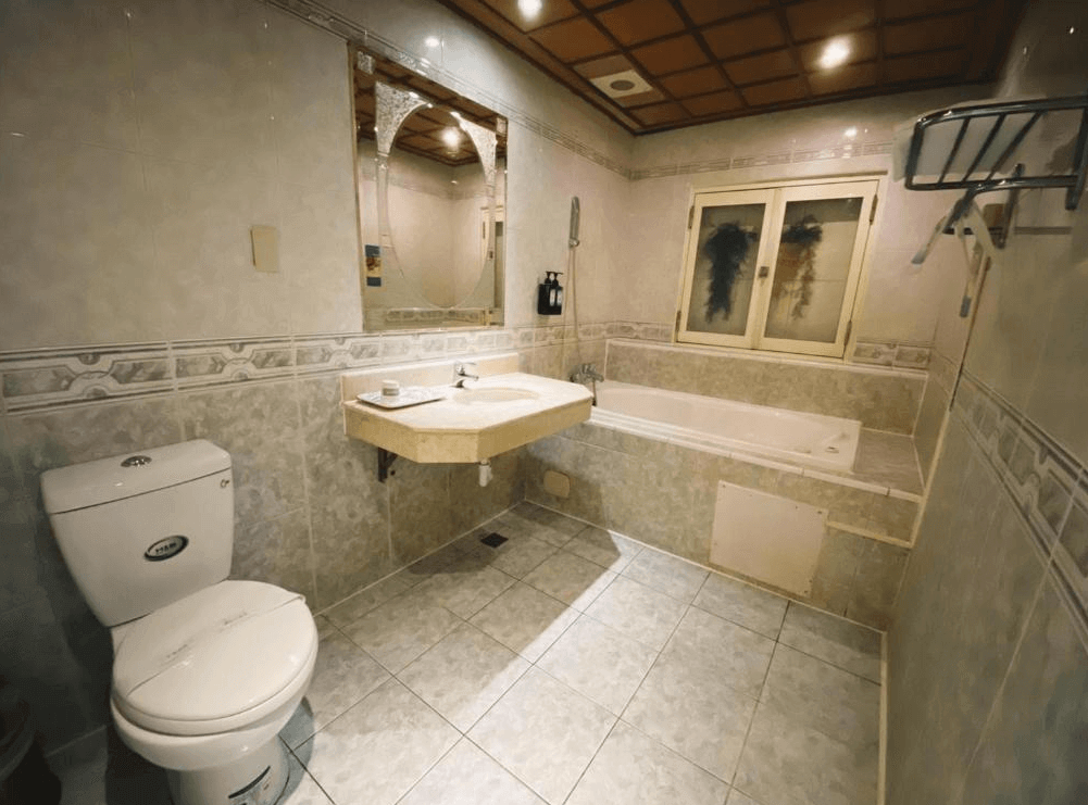 【高雄寵物友善住宿】艾萊商務汽車旅館的衛浴空間，設有浴缸、馬桶與洗手台，並配有鏡面與基本備品，空間寬敞實用，散發一種復古家常的氛圍。