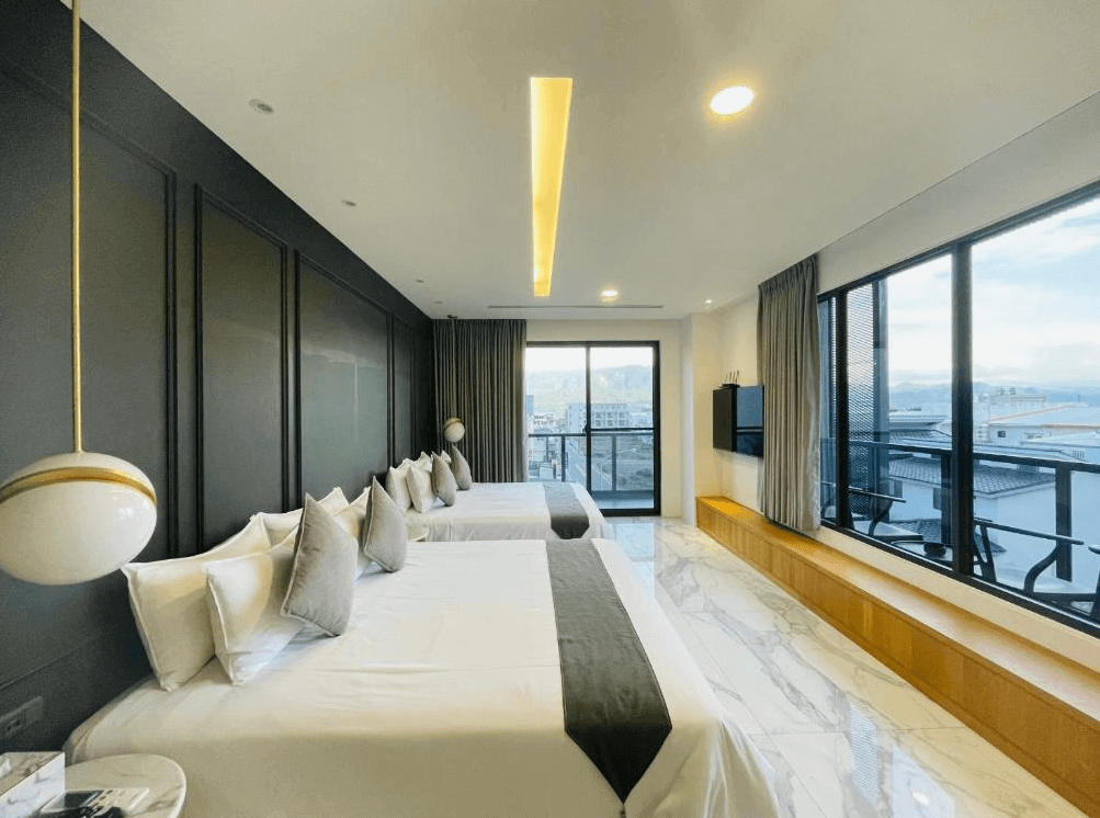 【關山住宿】茶田關舍二館的海景家庭房型，採用現代簡約風格設計，設有兩張大床與大片落地窗，可遠眺海景與城市景觀，地板為大理石質感材質，空間明亮寬敞。