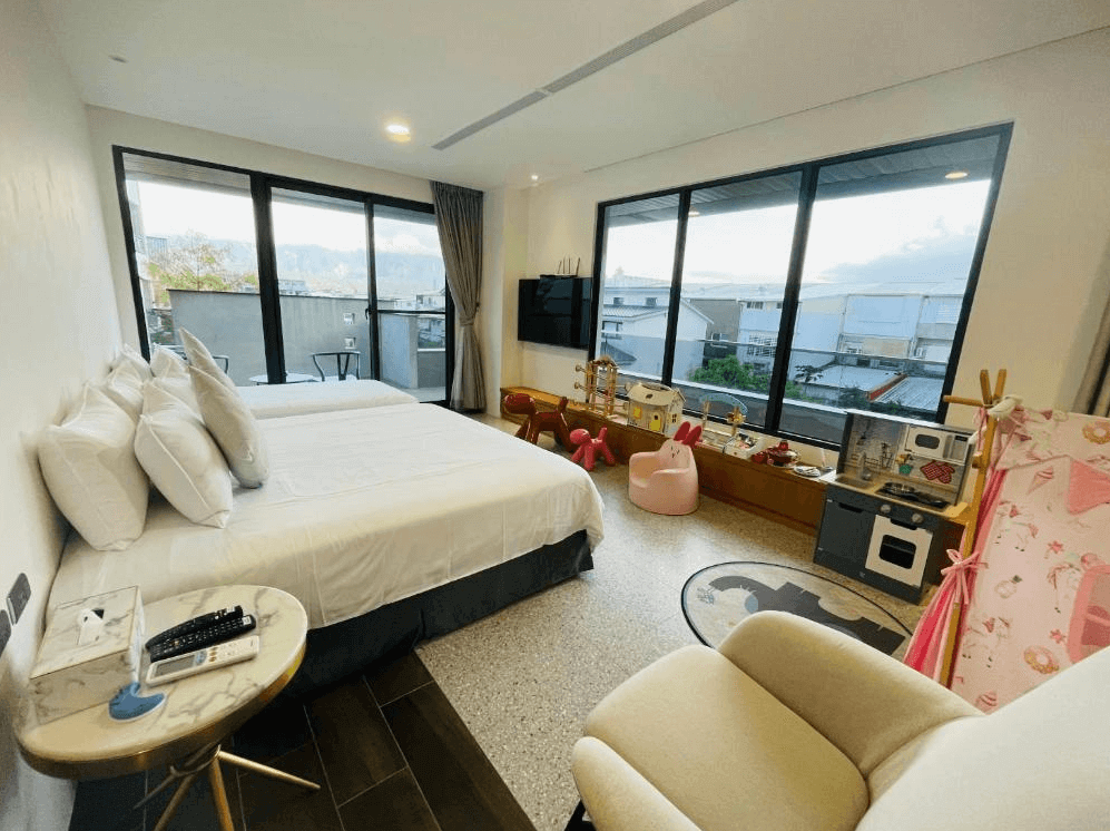 【關山住宿】茶田關舍二館的親子房型，配有一張大床與大量兒童玩具與廚具模型，窗外可看到市區景觀，適合親子共度悠閒時光。