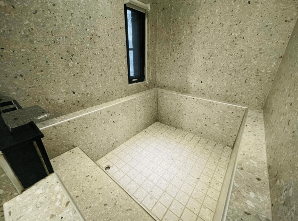 【關山住宿】茶田關舍二館設有寬敞石材泡湯池，採用磨石子紋理與落地窗設計，帶來簡約又放鬆的浴室空間，非常適合旅人泡湯放鬆。