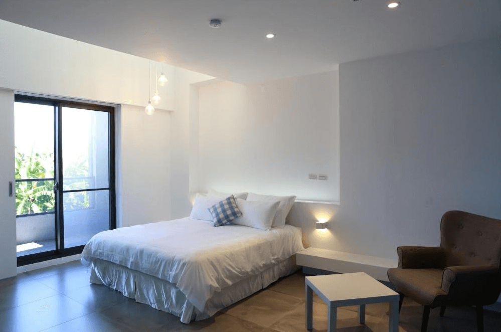 【關山住宿】茶田關舍民宿的一間簡約雙人房，設有白色床鋪、溫馨燈飾及大片窗戶，陽光灑入，空間明亮舒適。