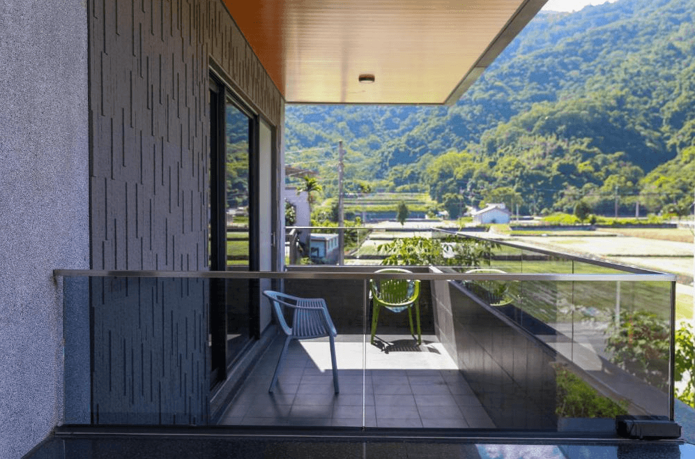 【關山住宿】茶田關舍民宿的戶外陽台，擁有玻璃圍欄與簡約椅子，可眺望前方稻田與遠山景色，享受寧靜田園風光。