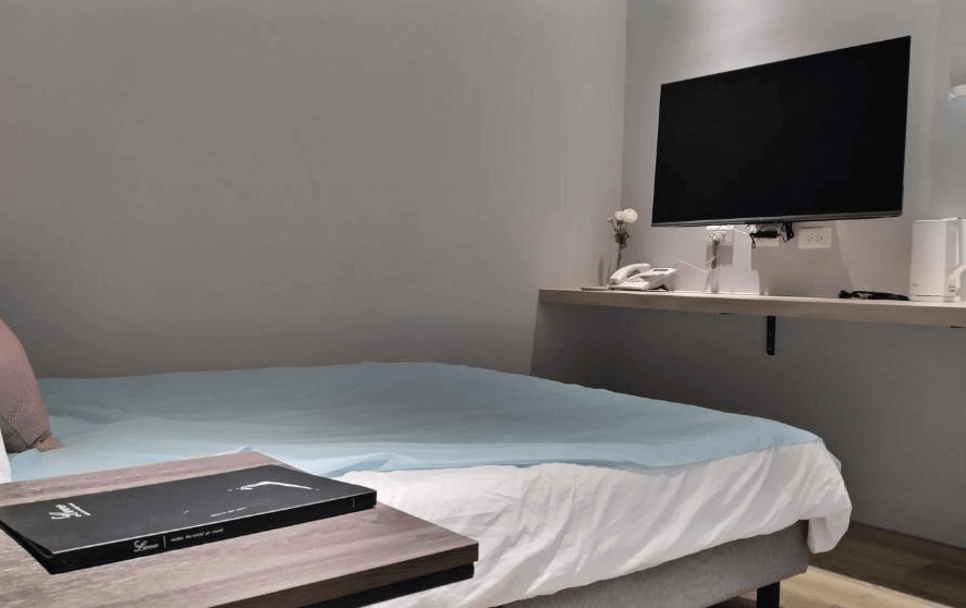 【高雄寵物友善住宿】蘆思特六合民宿的房內設計簡約俐落，配有一張雙人床、牆上安裝的平面電視及懸浮式桌面，桌上備有電話、熱水壺與茶杯，整體風格清新現代。