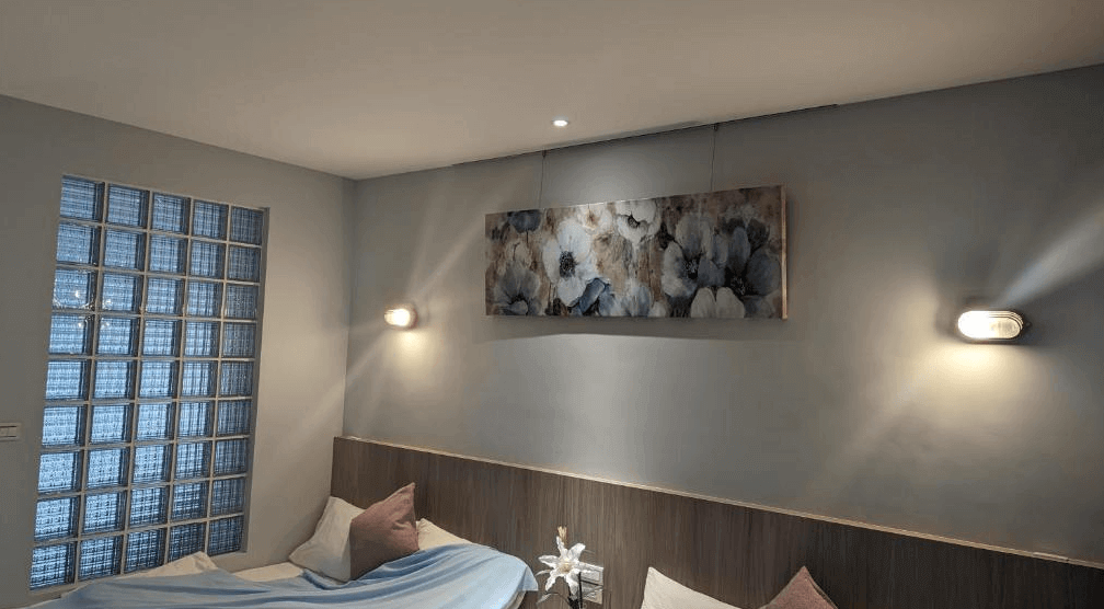 【高雄寵物友善住宿】蘆思特六合民宿的牆上掛有花卉風格畫作，搭配兩側柔光壁燈與玻璃磚窗，床鋪擺有抱枕與柔和色系床單，營造溫馨與放鬆的氛圍。