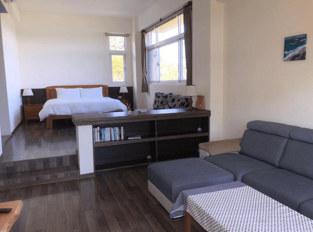 【東河住宿】蘭花楹海景民宿寬敞套房空間，設有加大雙人床、灰色沙發與閱讀區，中間隔有層架與書櫃，整體設計開放明亮，適合長住與家庭旅遊。