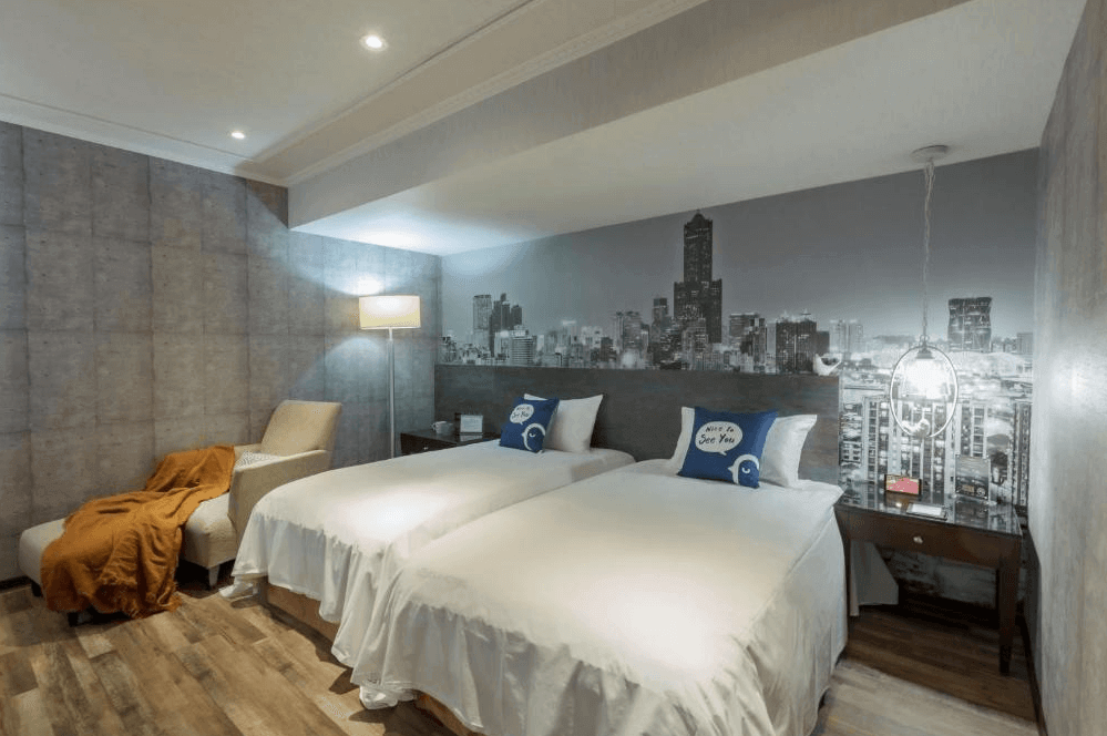 【高雄寵物友善住宿】西悠巢旅-高雄車站館的房內牆面以黑白城市夜景為背景，搭配雙人床與圓形吊燈，設有單人沙發與橘色毛毯，整體風格現代俐落，營造出都會旅宿的獨特氛圍。