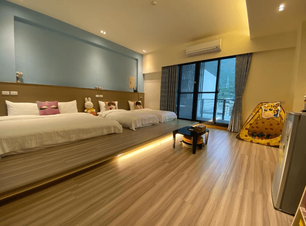 【關山住宿】"關山住宿精選示意圖"觀關嚮戶民宿的藍色主題家庭房，設有兩張大床與可愛玩偶擺設，右側配置動物造型小帳篷，適合親子入住，窗外可欣賞關山自然風光。