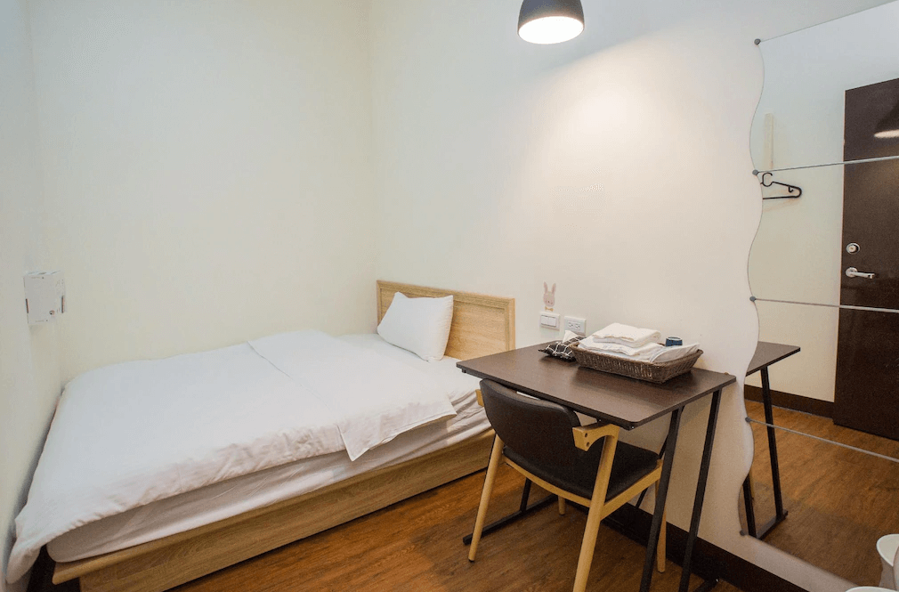 【Xpark住宿】豆子一家輕旅單人房，設有單人床與書桌，牆面配置曲線造型鏡與掛鉤，空間簡約實用，適合背包客或短期住宿旅客。