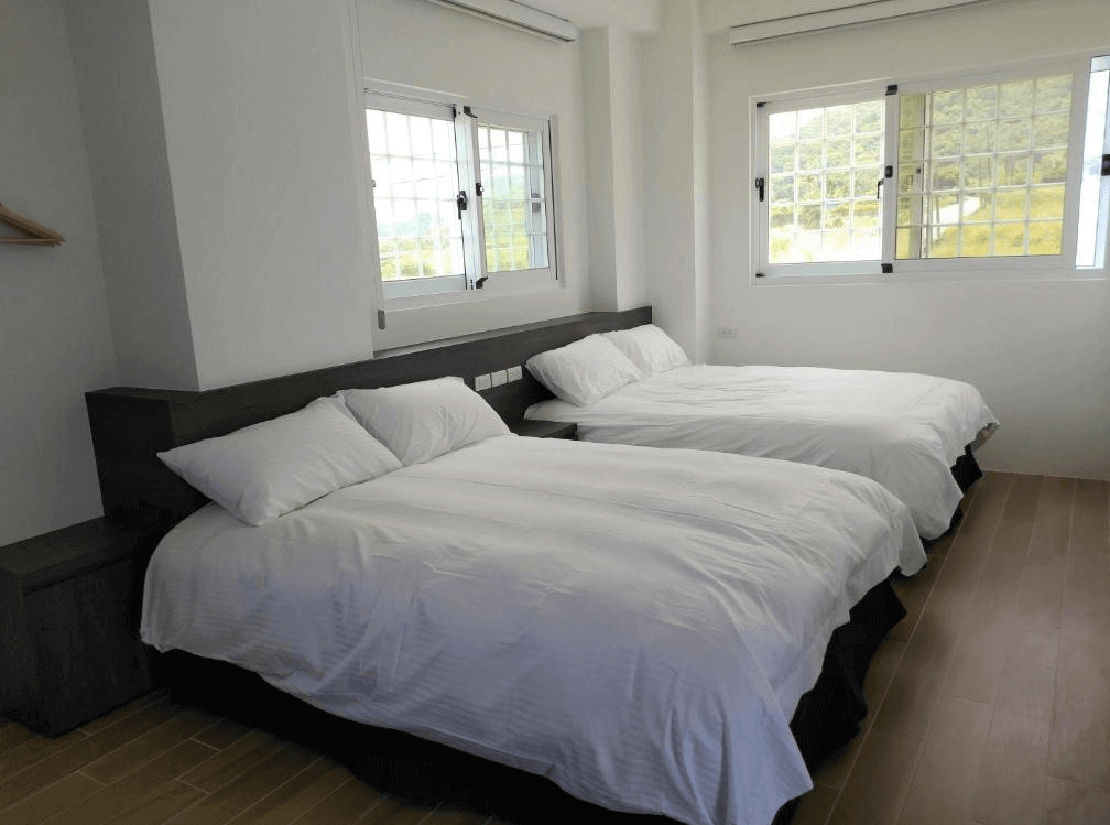 【長濱住宿】金剛大道民宿四人房，室內簡約明亮，設有兩張雙人床與大片窗戶，可欣賞戶外山景與稻田風光。