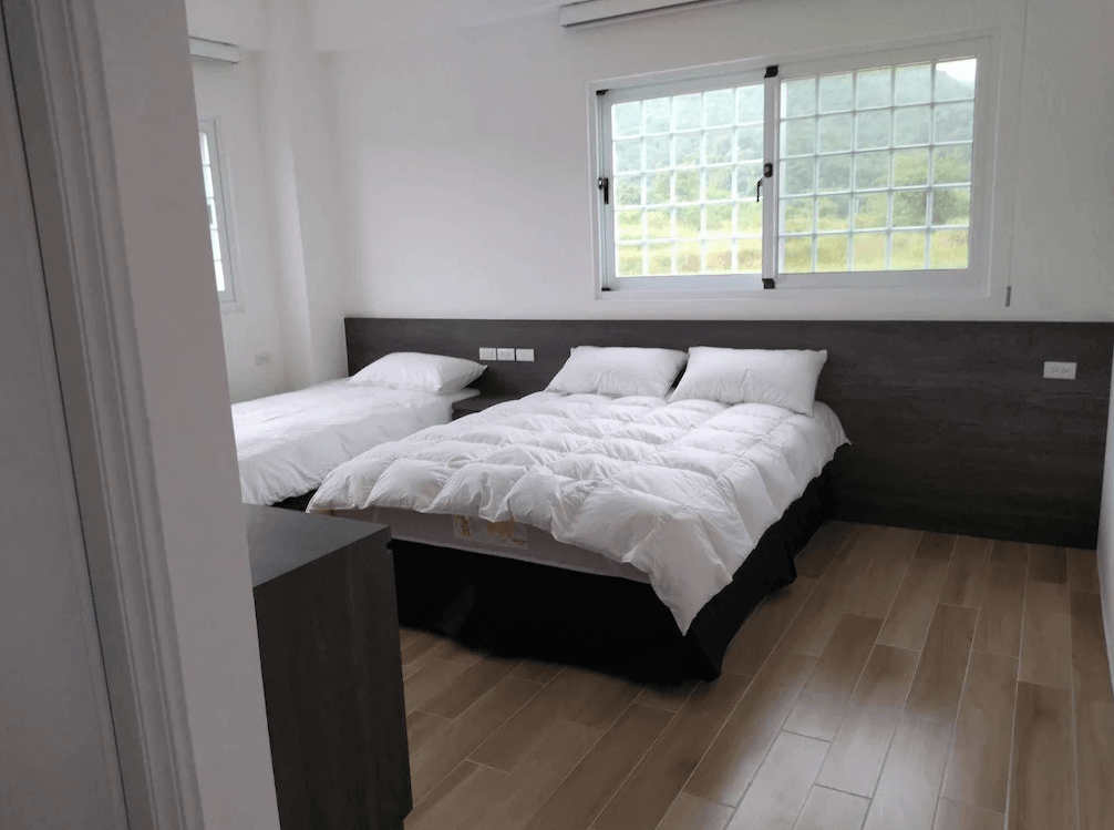 【長濱住宿】金剛大道民宿三人房，設有一張雙人床與一張單人床，搭配木地板與大片窗景，展現自然簡潔的住宿風格。