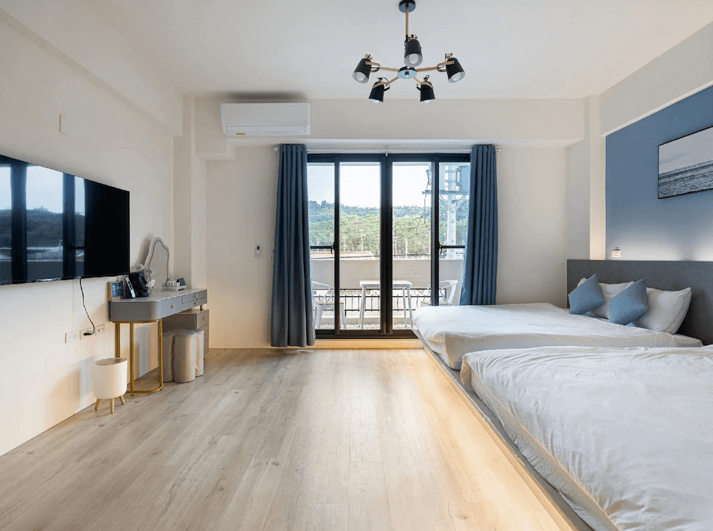 【玉井住宿】鈺景 NU TIME 的雙床家庭房，空間寬敞明亮，配有兩張舒適大床，設計以藍白色系為主，房內有大片落地窗與陽台可眺望山景，並配有化妝桌、平面電視與現代吊燈，整體氛圍簡約時尚。