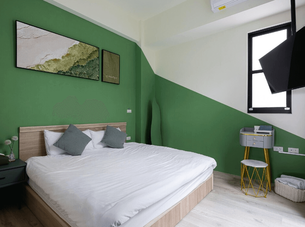 【玉井住宿】鈺景 NU TIME 的綠色主題雙人房，牆面採用綠白斜拼設計搭配自然風掛畫，木質床架與簡約床頭櫃營造溫馨感，角落設有梳妝桌與電視，充滿年輕清新的視覺感受。