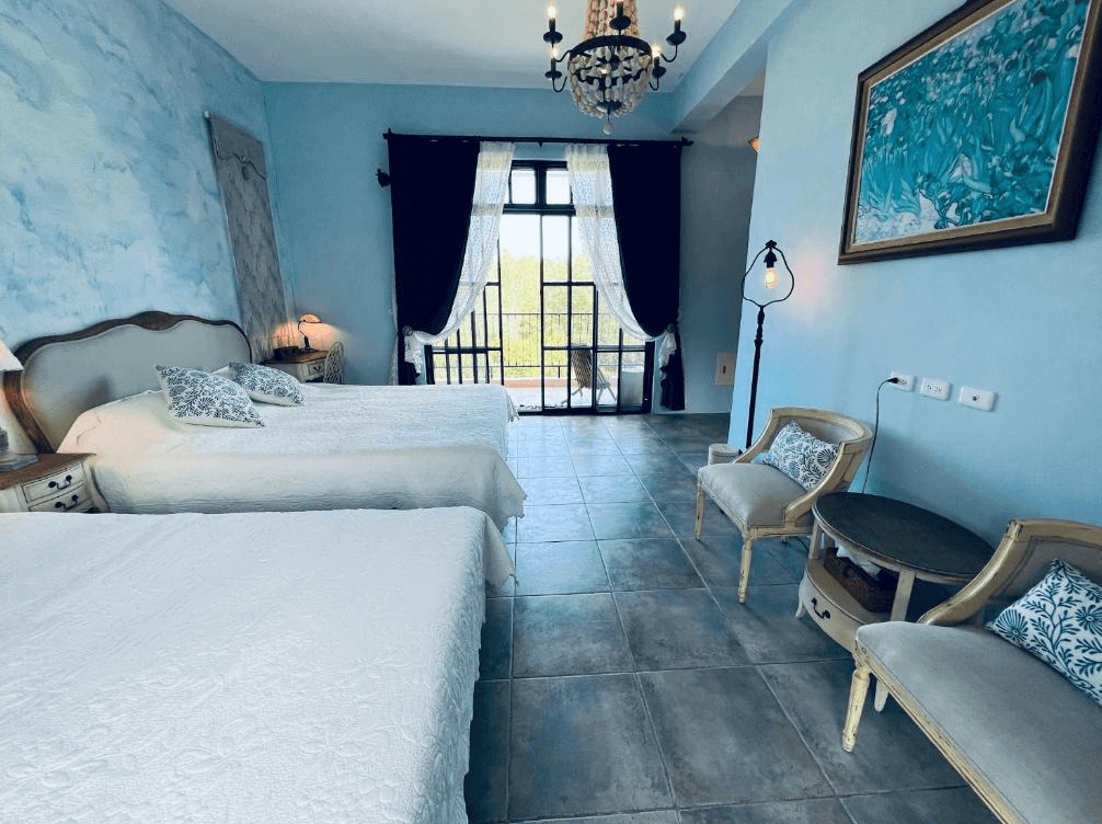 【長濱住宿】陌上草薰民宿鄉村風四人房，牆面以淡藍色手繪風格妝點，配有兩張雙人床、古典吊燈與法式座椅，大片落地窗引入自然光，充滿南法氛圍。