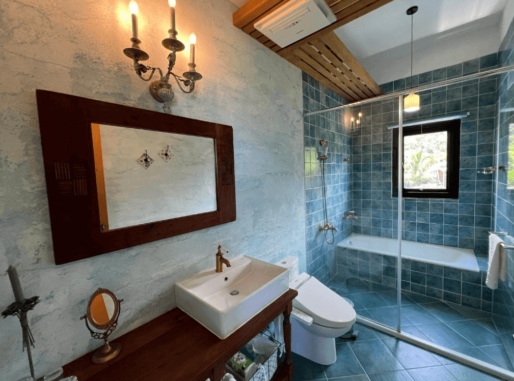 【長濱住宿】陌上草薰民宿復古浴室，採用湖水藍色磁磚與玻璃乾濕分離設計，設有浴缸與金屬壁燈，營造懷舊且清新的沐浴空間。