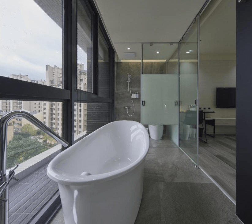 【Xpark住宿】青埔商旅景觀浴缸房型，獨立白色浴缸設於大片落地窗旁，浴室空間寬敞明亮，設有淋浴與玻璃隔間馬桶，享受泡澡時的城市景色。