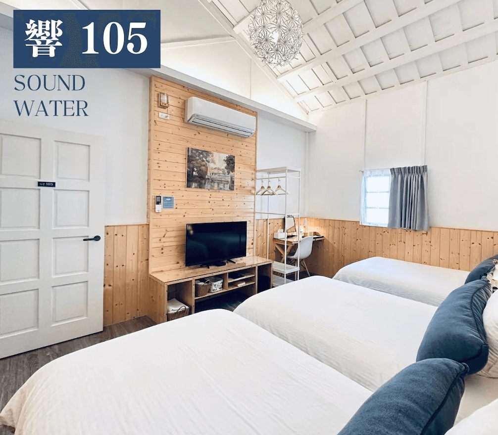 【苗栗包棟民宿】響水客棧的溫馨木質牆面與白色挑高天花設計，搭配三張單人床與簡約書桌、電視，整體風格清新明亮，適合家庭或朋友同行入住。