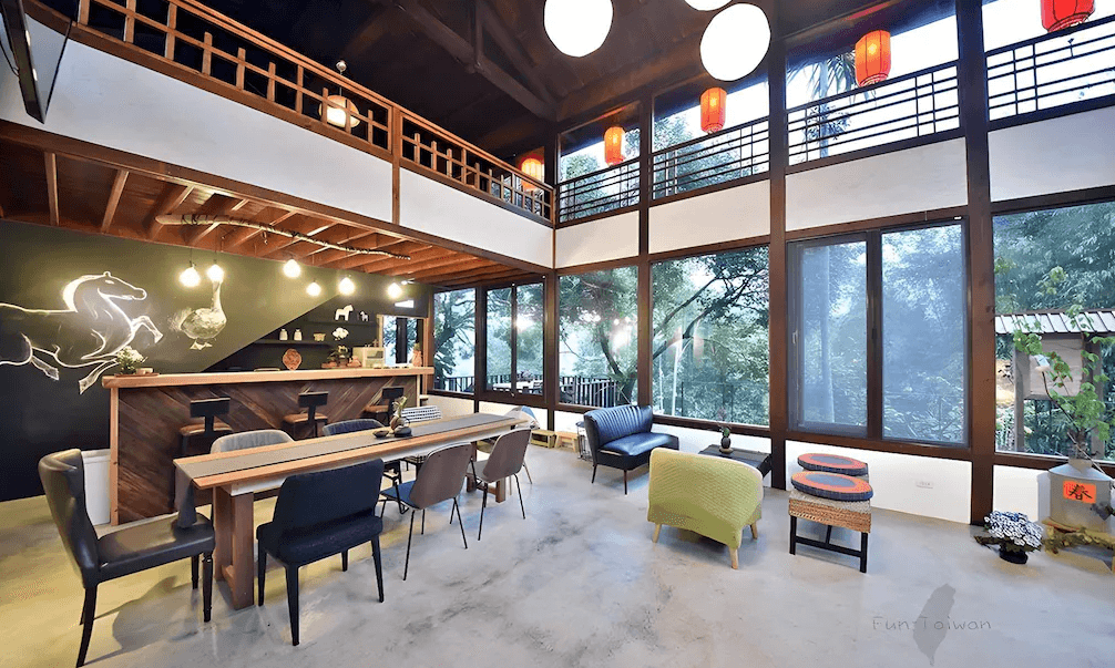 【苗栗包棟民宿】響水客棧擁有大片落地窗與挑高設計的開放式交誼廳，搭配原木長桌、吧檯與多款沙發座椅，牆上繪有馬與鵝的插畫，環境充滿自然與藝術氛圍。
