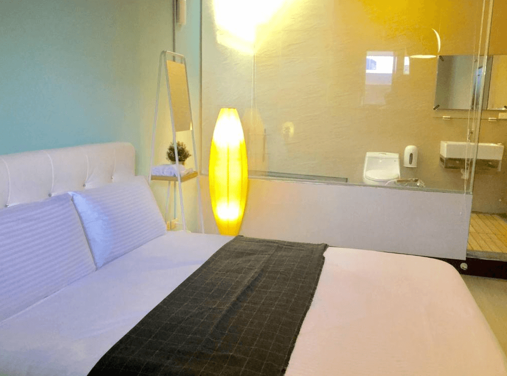 【Xpark住宿】高鐵背包客 HSR B&B 雙人房，房內床鋪對面為半透明玻璃隔間衛浴，搭配柔和燈光與時尚立燈，營造現代簡約風格。