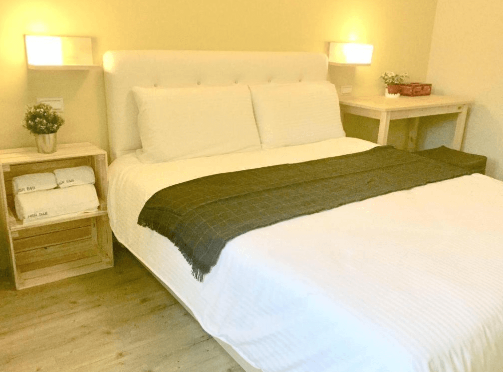 【Xpark住宿】高鐵背包客 HSR B&B 雙人房，設有柔白床鋪與木質家具，床邊擺放毛巾與盆栽，營造出自然溫馨的住宿空間。