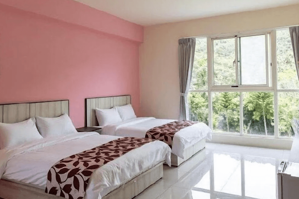 【苗栗包棟民宿】麥克尼景觀莊園的四人房配置兩張雙人床，粉色牆面搭配大片窗景，透進自然光線與山林綠意，非常適合親子或朋友同行入住。