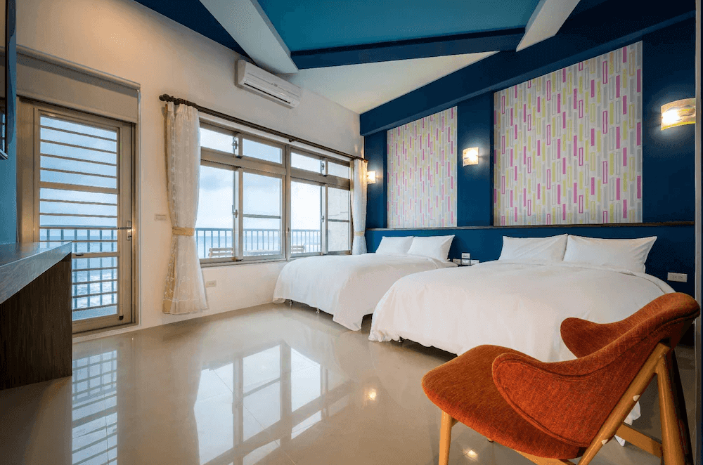 【長濱住宿】默砌旅店東海灣民宿四人海景房，兩張大床設於藍色主牆前，落地窗外可遠望海岸線，房內採光充足，設計溫馨活潑。