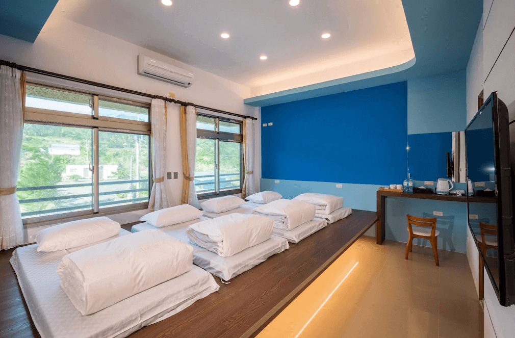 【長濱住宿】默砌旅店東海灣民宿日式通舖房型，鋪設六組床墊，適合家庭或團體入住，牆面以清新的藍色點綴，窗外可見綠意山景。