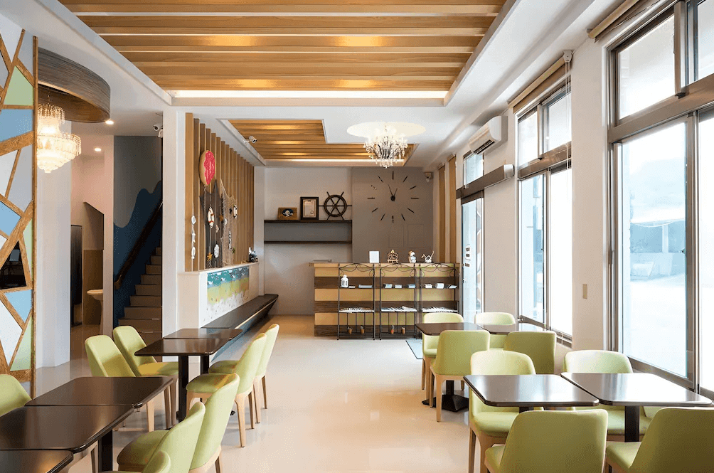 【長濱住宿】默砌旅店東海灣民宿公共用餐區，裝潢明亮寬敞，木質天花板與大面窗戶增添自然感，綠色座椅與裝飾提升空間活潑氛圍。