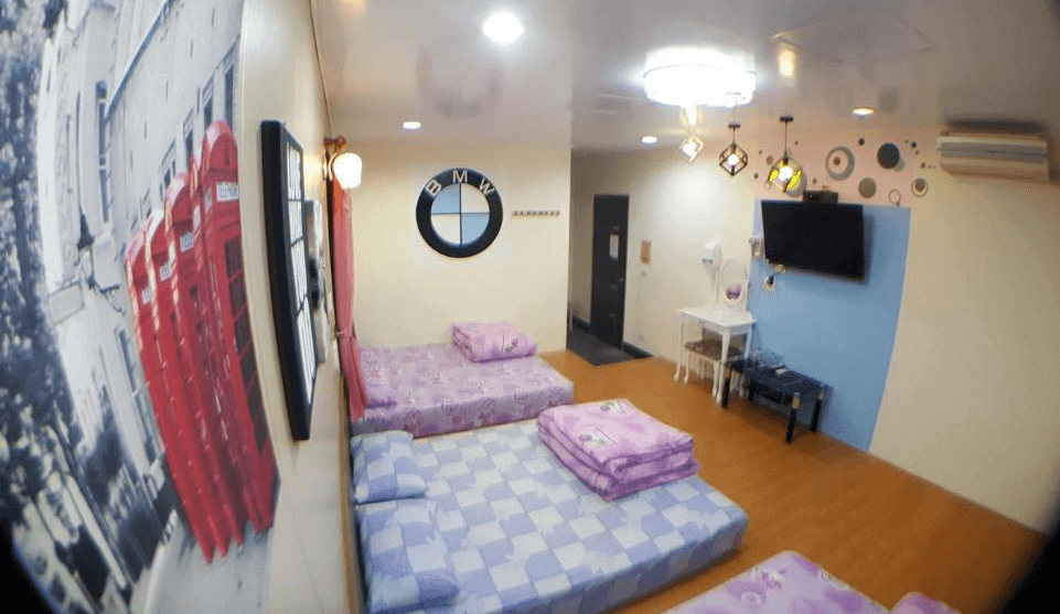 【布袋住宿】龍園旅館多人大通鋪房，擺放三張地墊床組，床鋪排列整齊，牆上有BMW車標裝飾與倫敦紅色電話亭壁畫，風格輕鬆趣味，另設有電視與梳妝台。