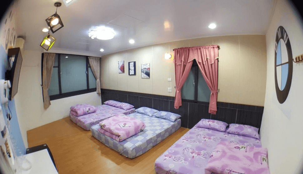 【布袋住宿】龍園旅館六人通舖房整體視角，三張床墊整齊排放，搭配粉紅與灰色床被，牆上裝飾有英文字畫與汽車海報，右側牆面有BMW標誌與粉紅色窗簾，適合家庭或團體入住。