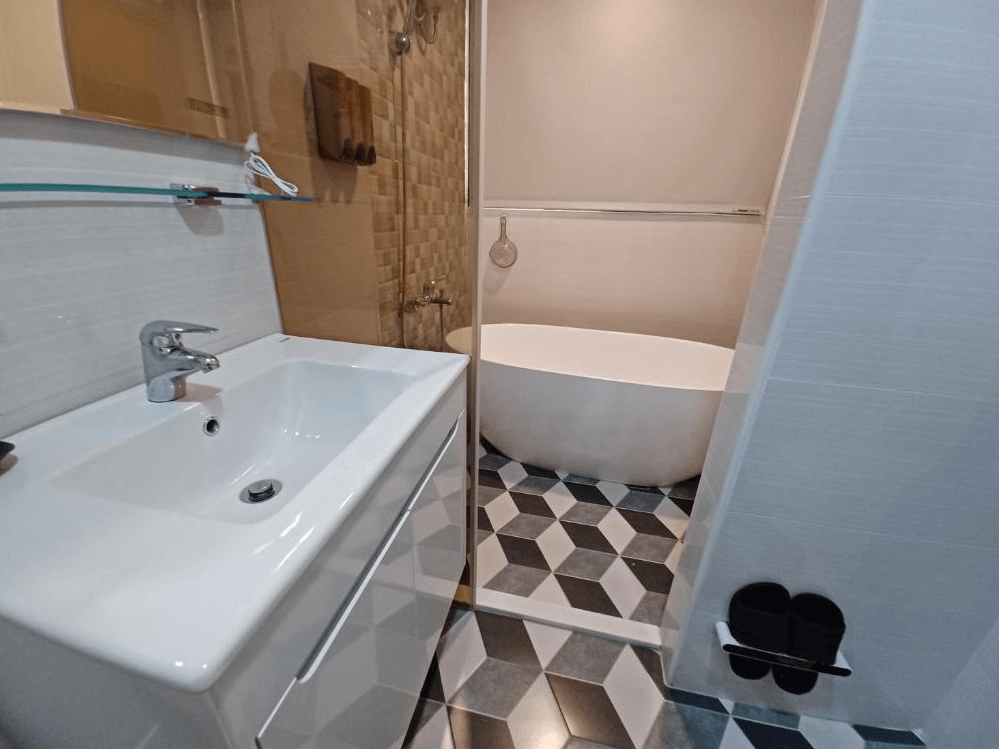 【古坑住宿】111古坑行旅的衛浴設施，設有現代感洗手台、玻璃隔間淋浴區及獨立蛋形浴缸，搭配幾何花磚地板，整體設計簡潔有型。