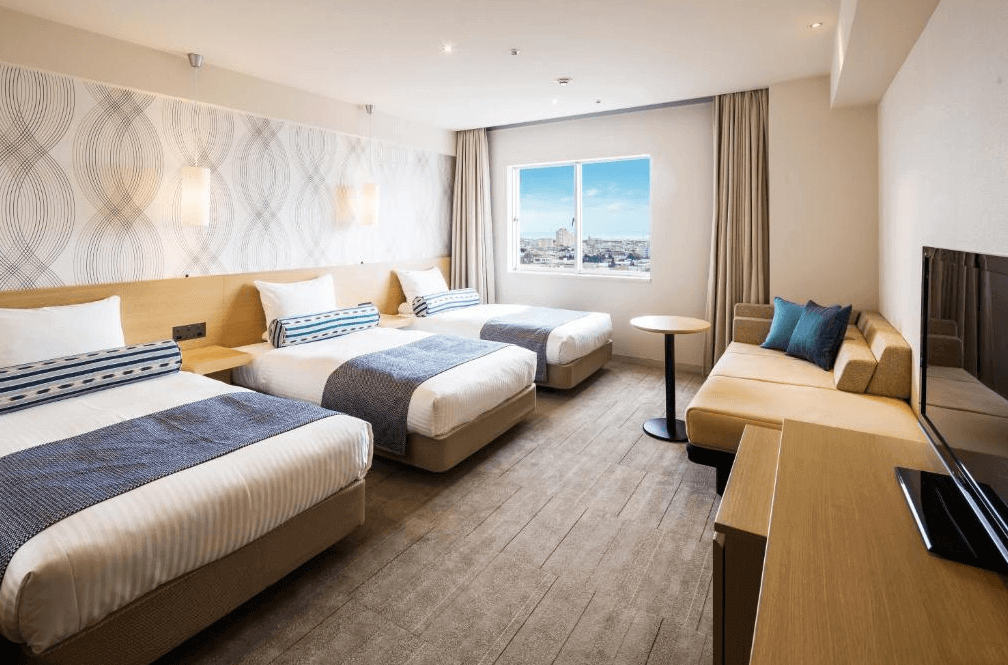 【石垣島住宿】ART石垣島酒店三人房，配有三張單人床與沙發區，室內設計明亮寬敞，適合全家人或朋友同住，窗外可眺望城市景致。