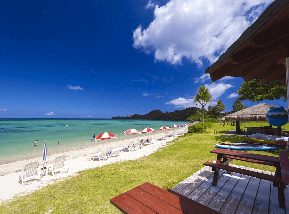 【石垣島住宿】Ishigaki Seaside Hotel 專屬白沙灘區，整排遮陽傘與沙灘躺椅迎向清澈海水，草地區還設有木桌椅與涼亭，非常適合親子與海灘活動。