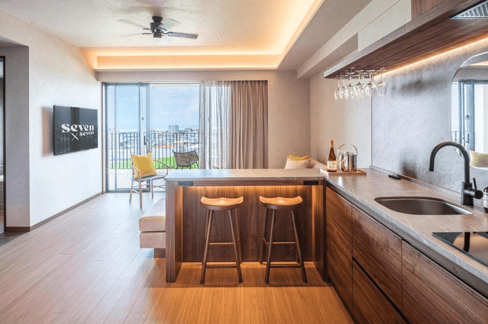 【石垣島住宿】seven x seven ISHIGAKI設有開放式廚房與吧檯空間，搭配玻璃酒杯吊架與陽光灑落的客廳座位區，溫馨又實用。