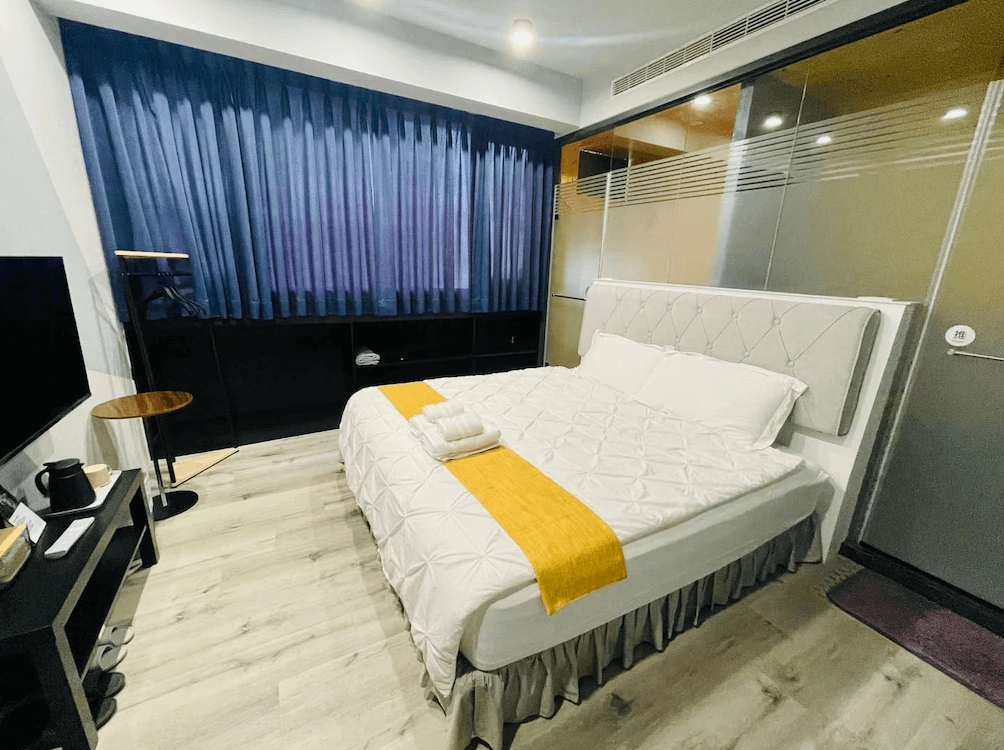 【竹山住宿】一瓢食宿溫馨雙人房，鋪設木地板並搭配沉穩深藍窗簾，房內配有電視、電熱水壺與簡約書桌，床鋪擺放整齊，環境整潔舒適。