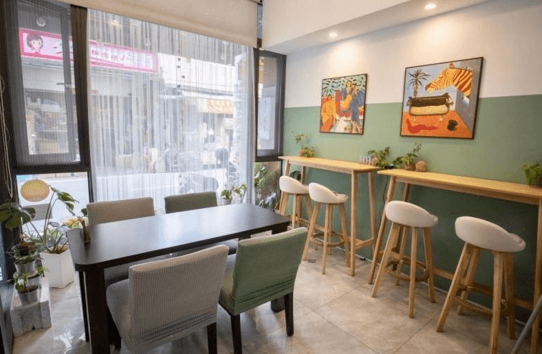 【竹山住宿】一瓢食宿一樓公共用餐區，擁有大片落地窗採光，擺設高腳桌椅與長桌，牆面掛有插畫風藝術畫作，整體風格簡約溫馨，適合旅人用餐與交流。